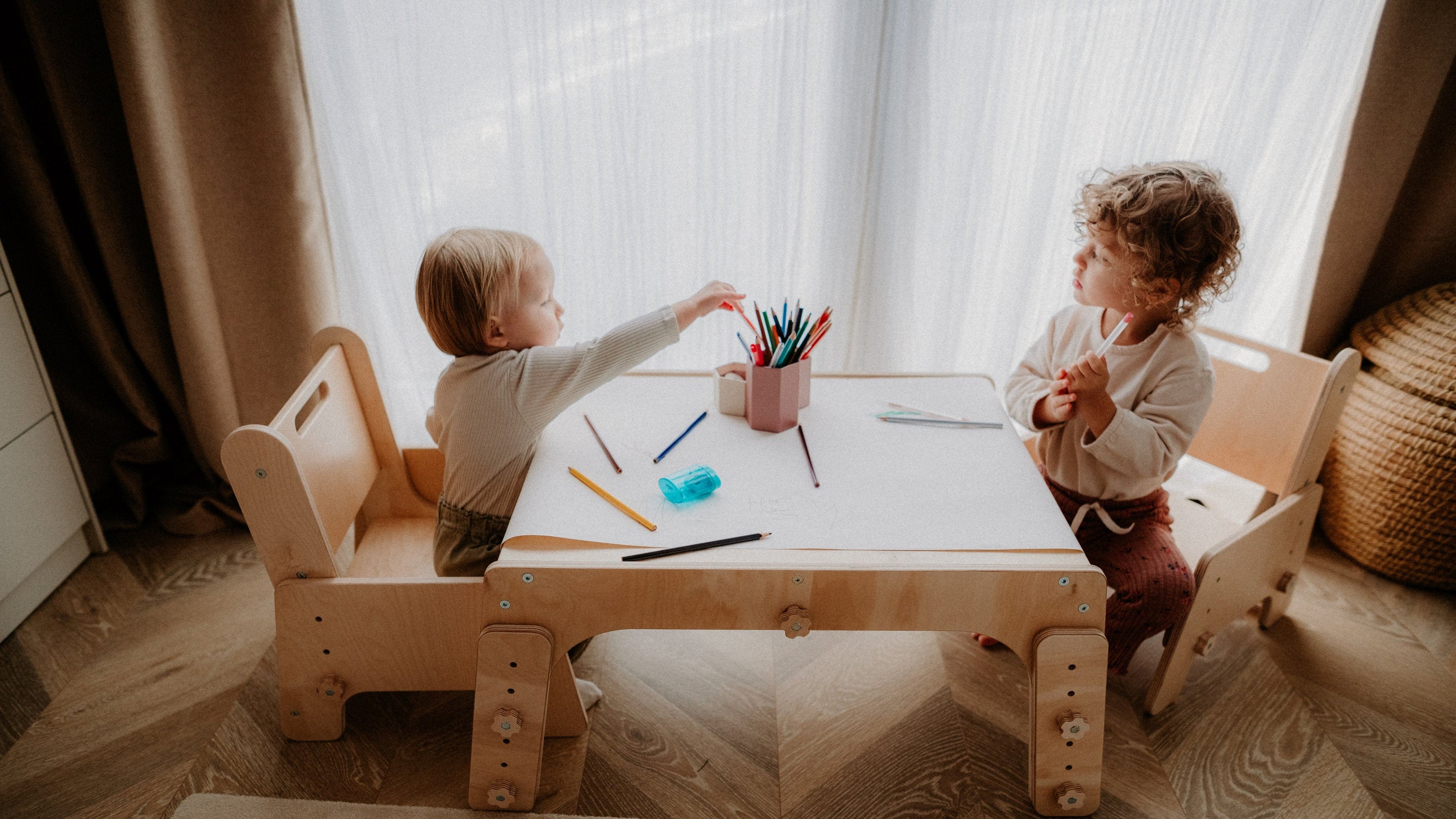 Two children sitting at a small table with art supplies in a cozy room.